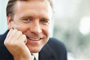 RABC-CCCR - A man in a suit smiling warmly at the camera, resting his chin on his hand. The background is softly blurred, giving a professional and approachable impression.