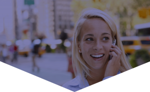RABC-CCCR - A smiling woman with blonde hair talks on a cellphone while standing outdoors in a city. The blurred background shows buildings, trees, and yellow taxis, suggesting an urban setting.